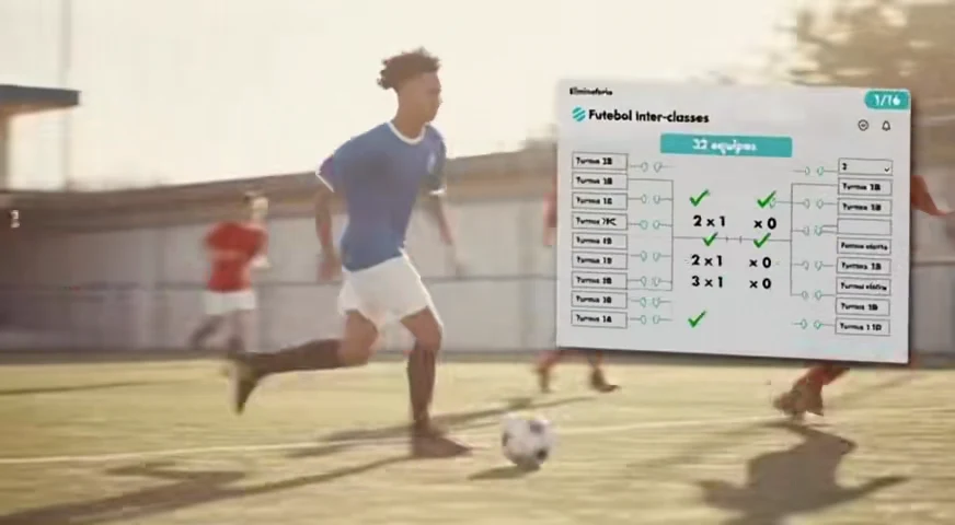 Um aluno conduz a bola no campo, com a chave do campeonato ao lado.