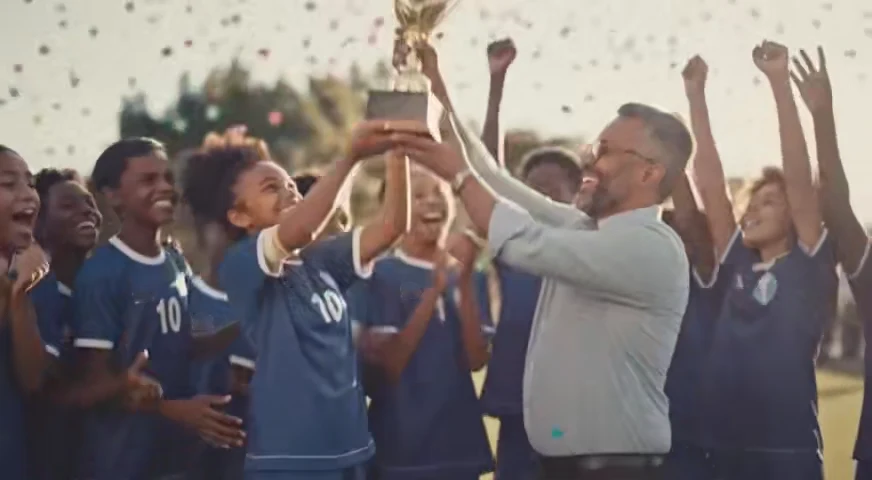 O time campeão levanta a taça junto com o professor, sob uma chuva de confete.